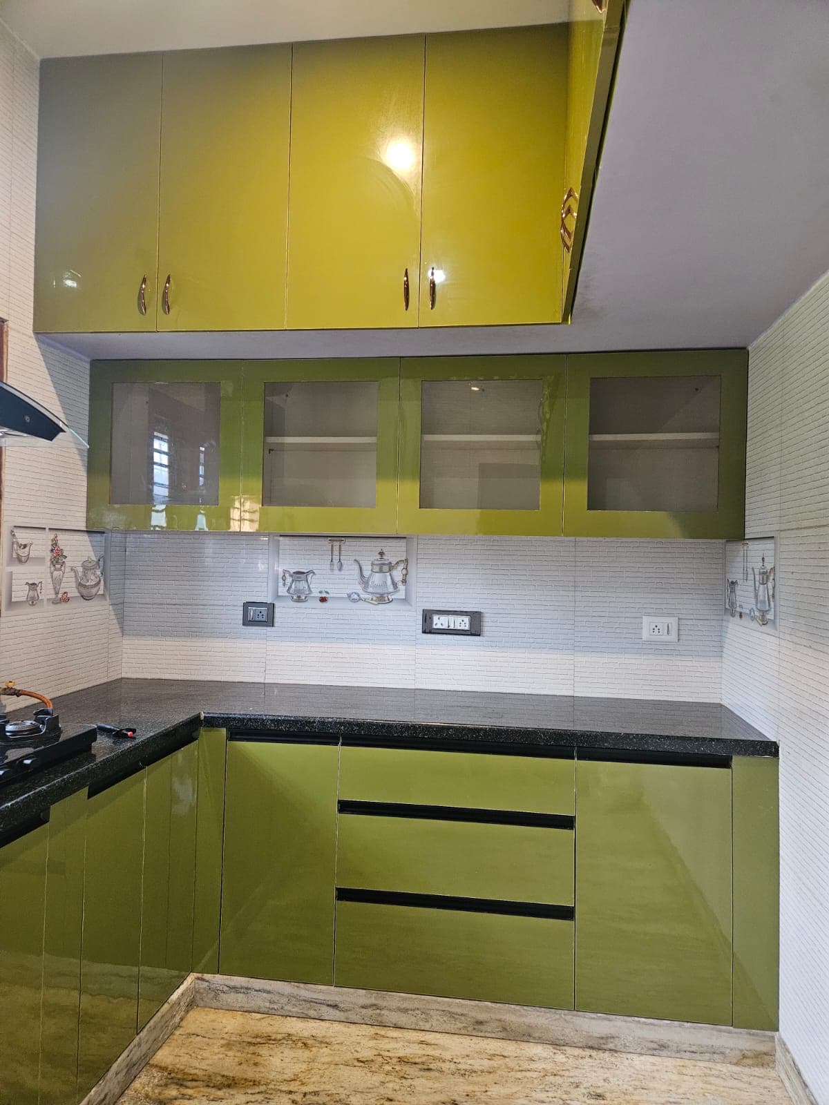The full L-shaped run of an olive-green gloss modular kitchen, with tall wall units above